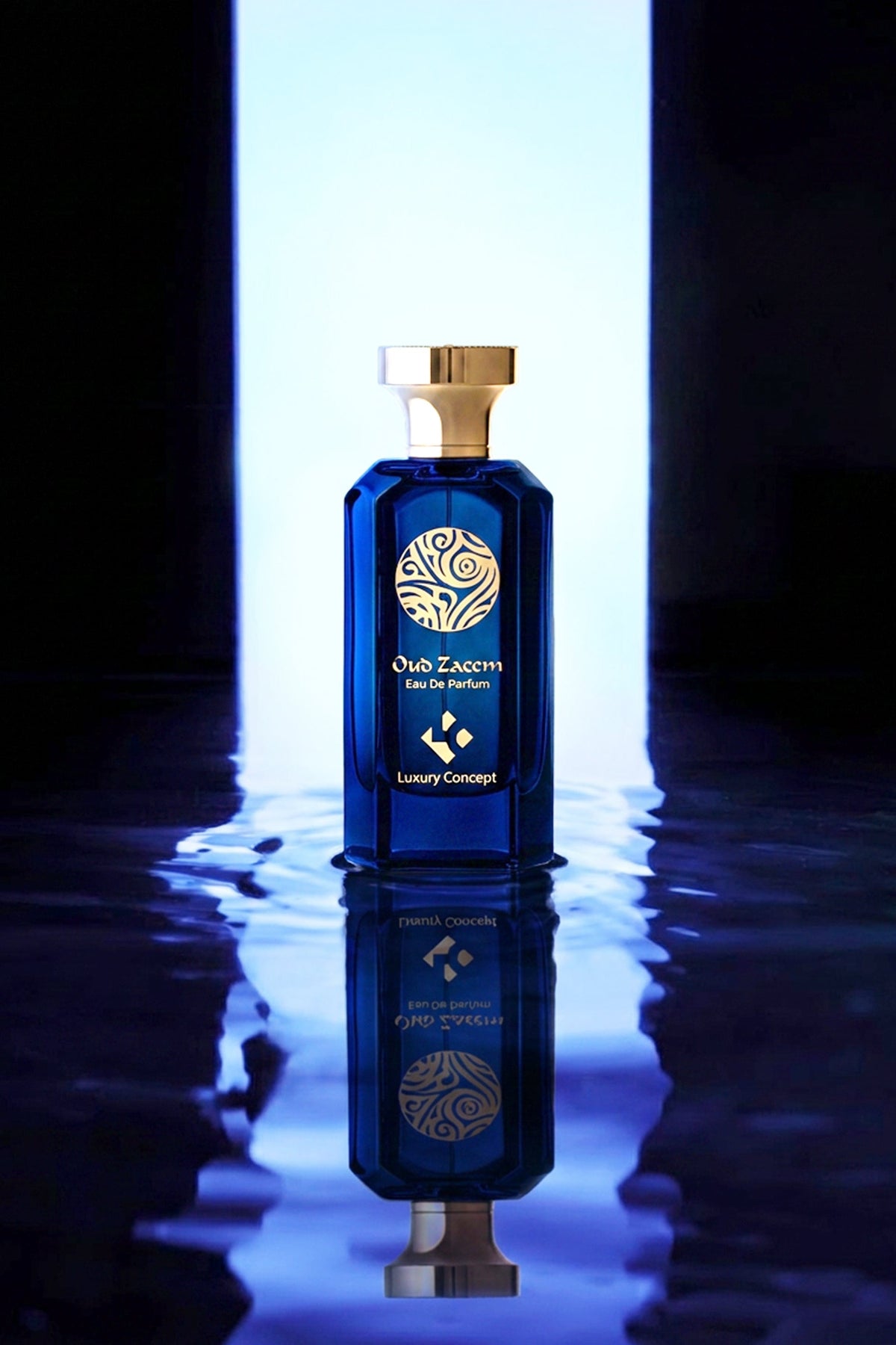 A luxury blue glass perfume bottle with a gold cap and gold logo, standing on a reflective dark surface with a bright vertical light behind it.