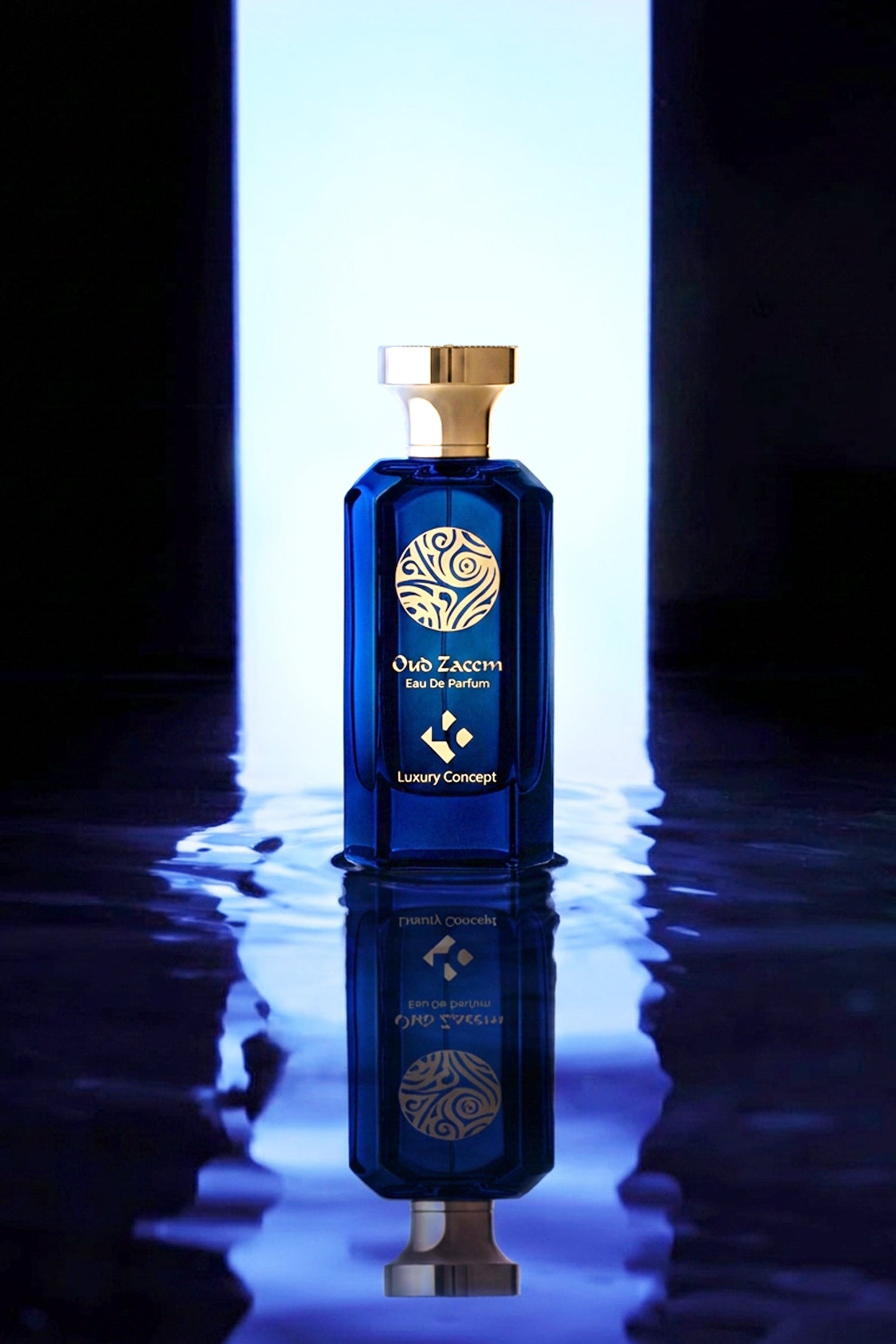 A luxury blue glass perfume bottle with a gold cap and gold logo, standing on a reflective dark surface with a bright vertical light behind it.